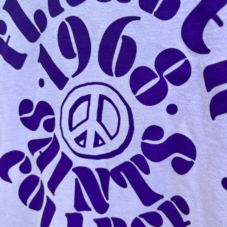 Lilac t-shirt with dark purple imprint saying Flagler over 1968 over peace sign design over Saints over College