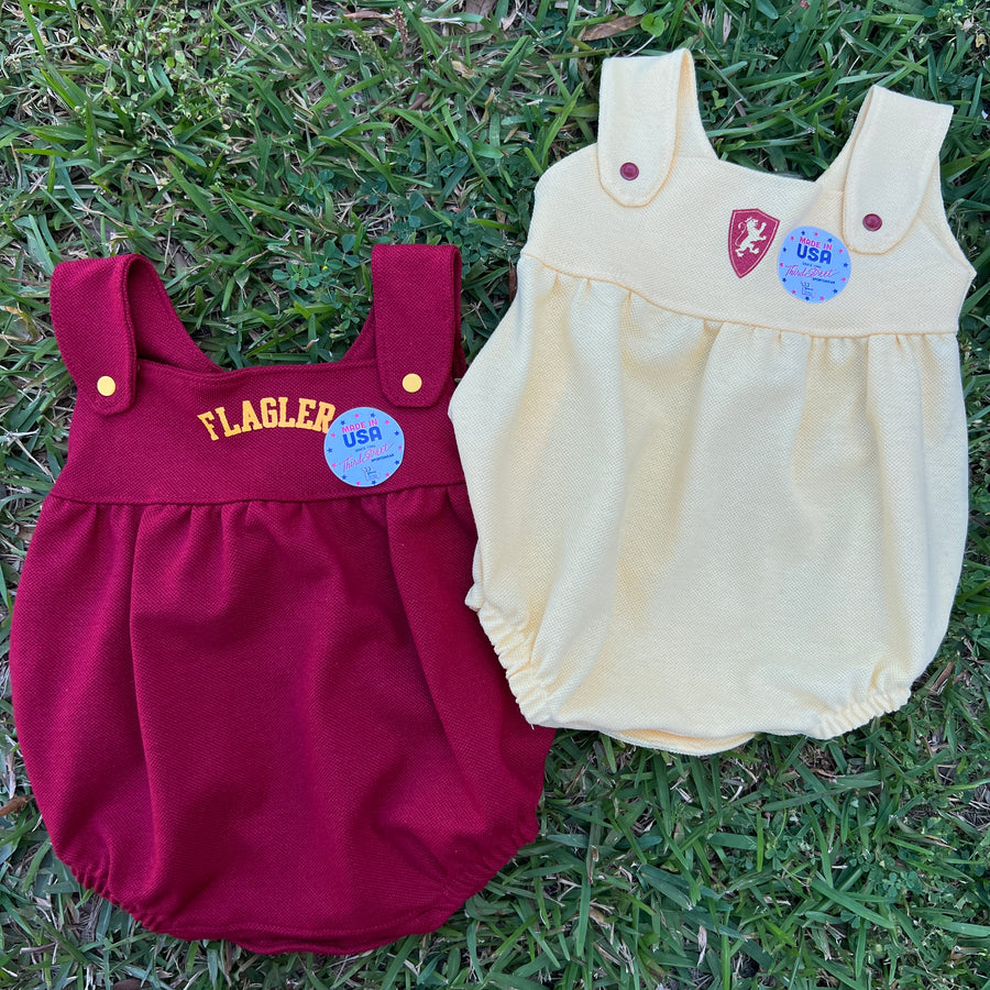Yellow bubble romper with overall straps with red buttons with Flagler college shield logo in top center