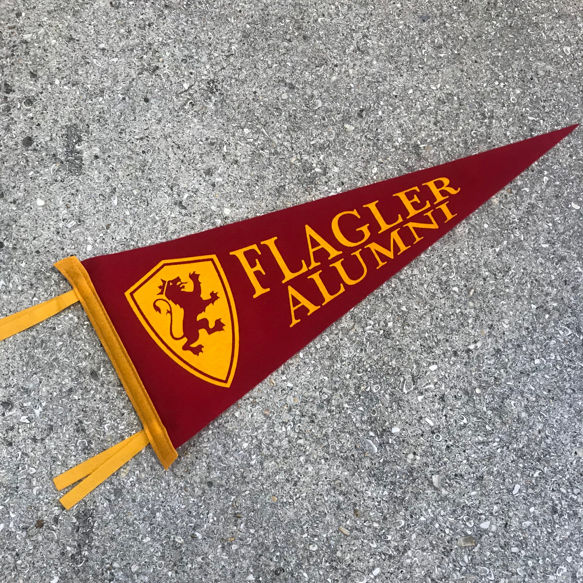 Crimson red pennant with Yellow Flagler College shield logo  to the left of imprint saying Flagler over Alumni