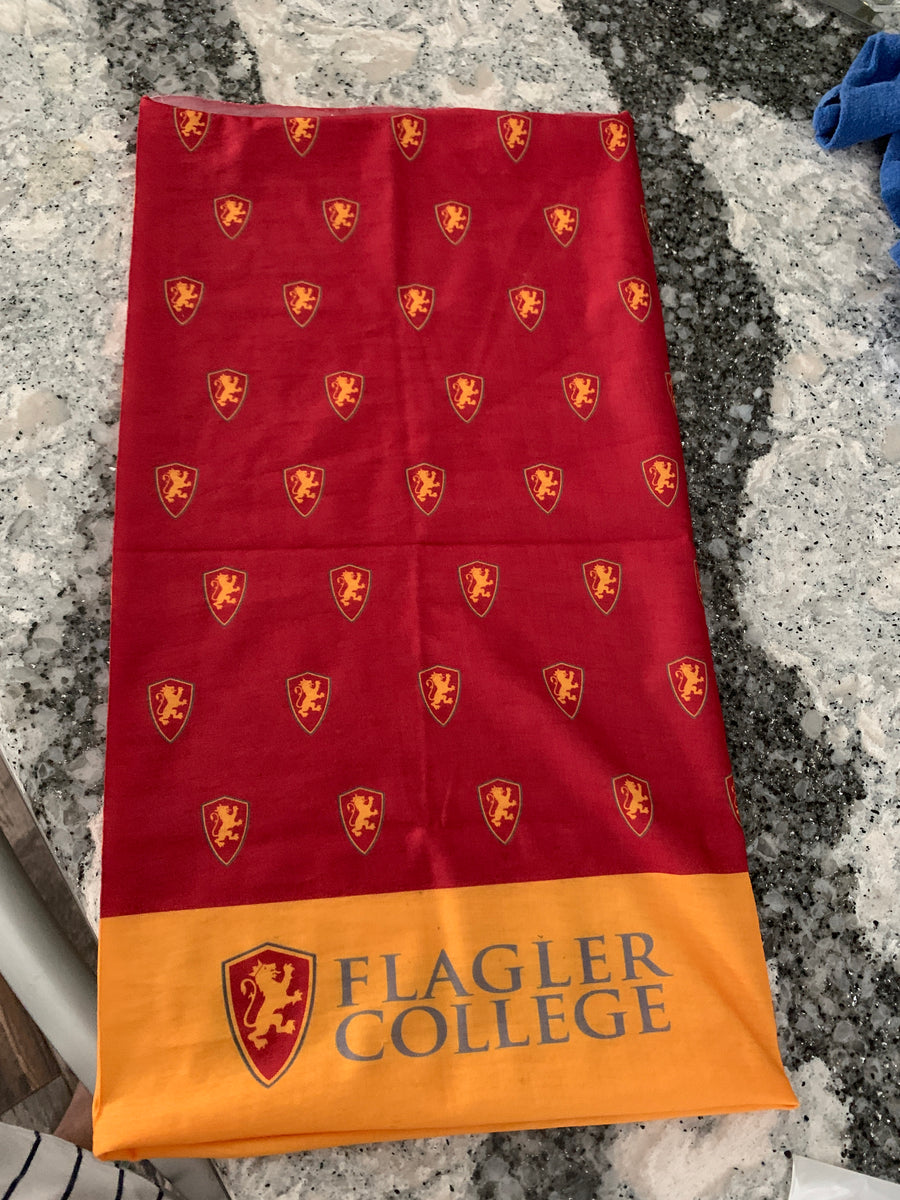 Gator next to packaging. Red fabric with flagler college shield logos over yellow bottom with big Flagler College shield next to grey letters saying Flagler over College