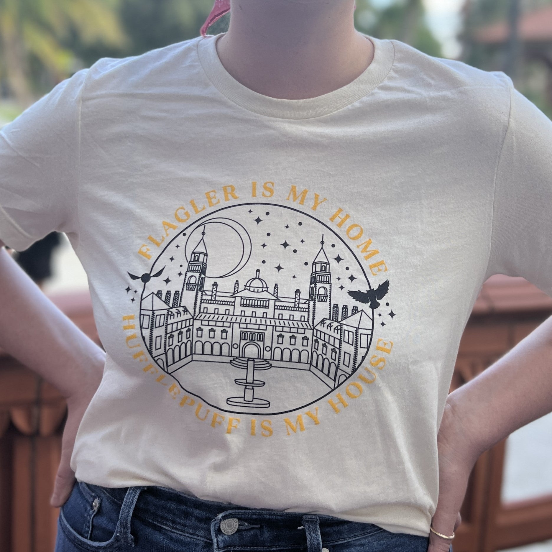 Natural t-shirt with yellow imprint saying Flagler Is My Home over black outline of Ponce de Leon over yellow imprint saying Hufflepuff Is My House