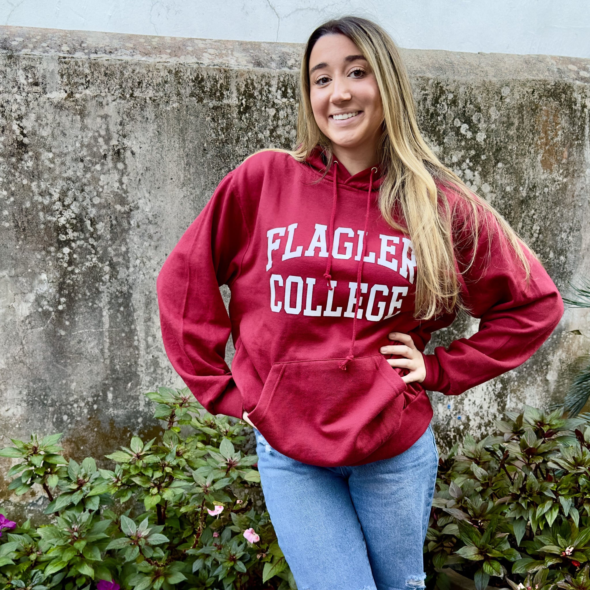 Woman wearing crimson solid hooded sweatshirt with white imprint saying Flagler over College