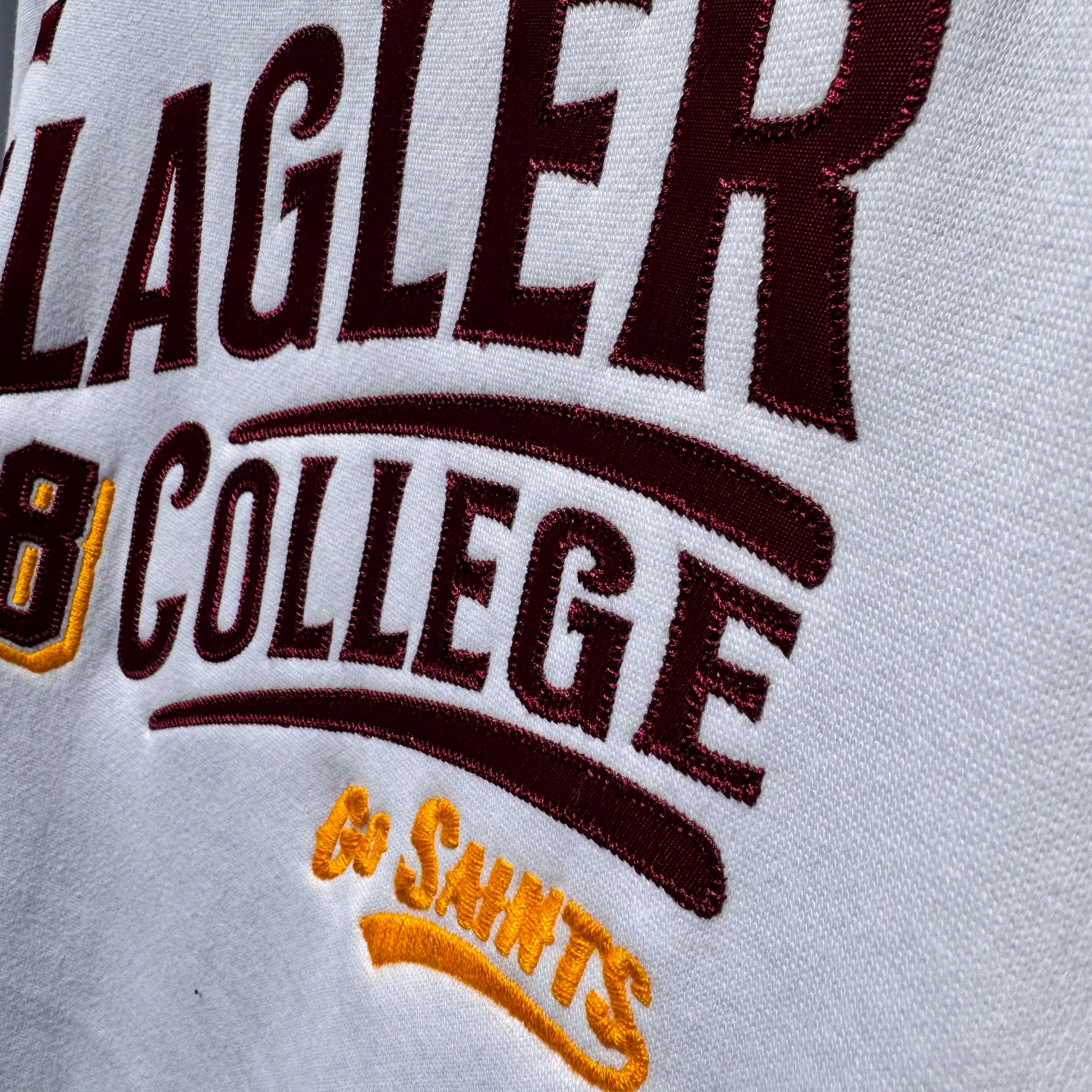 zoomed in photo of white solid crewneck with crimson imprint saying Flagler College over yellow imprint saying go saints
