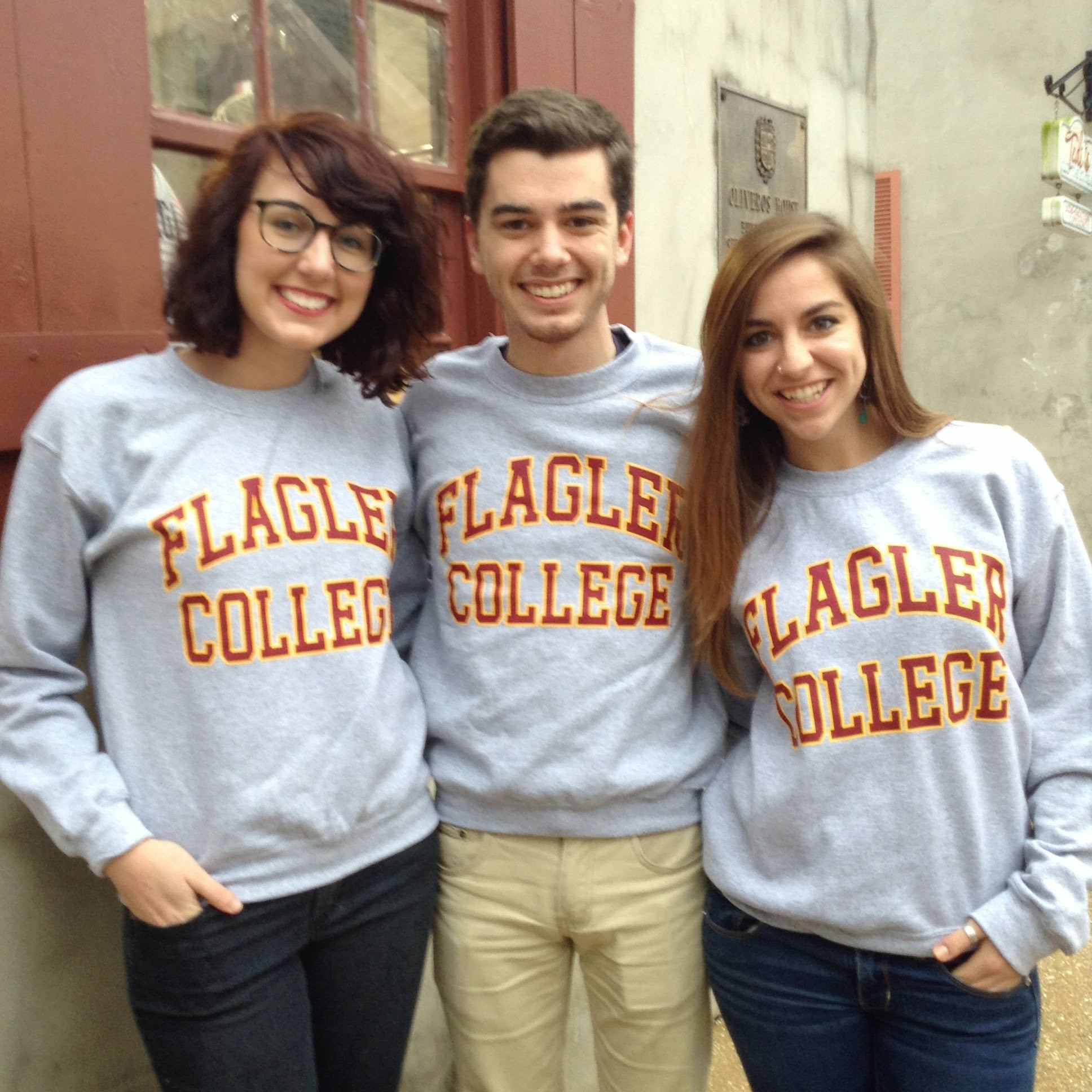 Three individuals wearing grey crewnecks with crimson imprint saying Flagler over College
