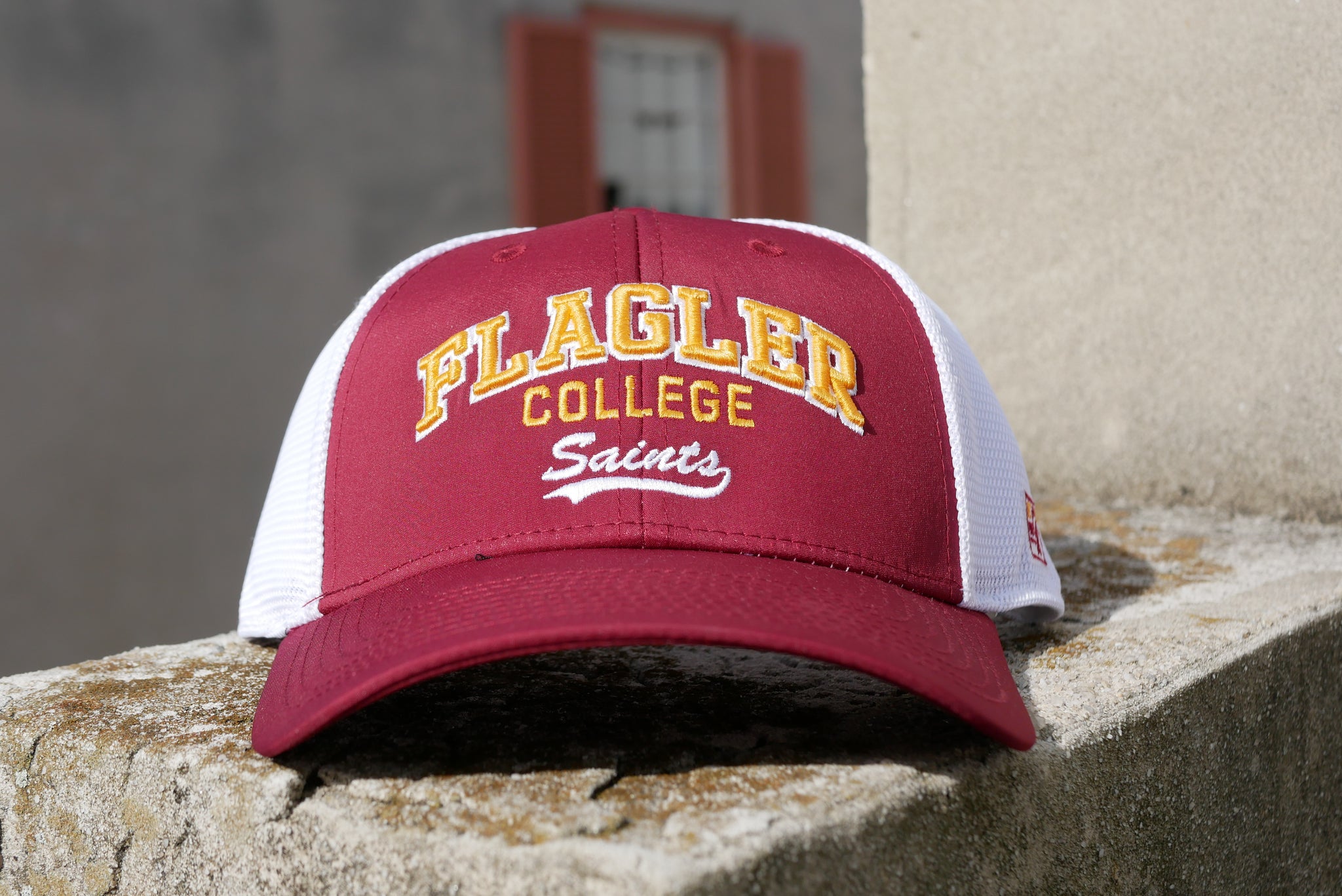 Red hat with mesh white back. Yellow embroider saying Flagler over College over white cursive embroider saying Saints