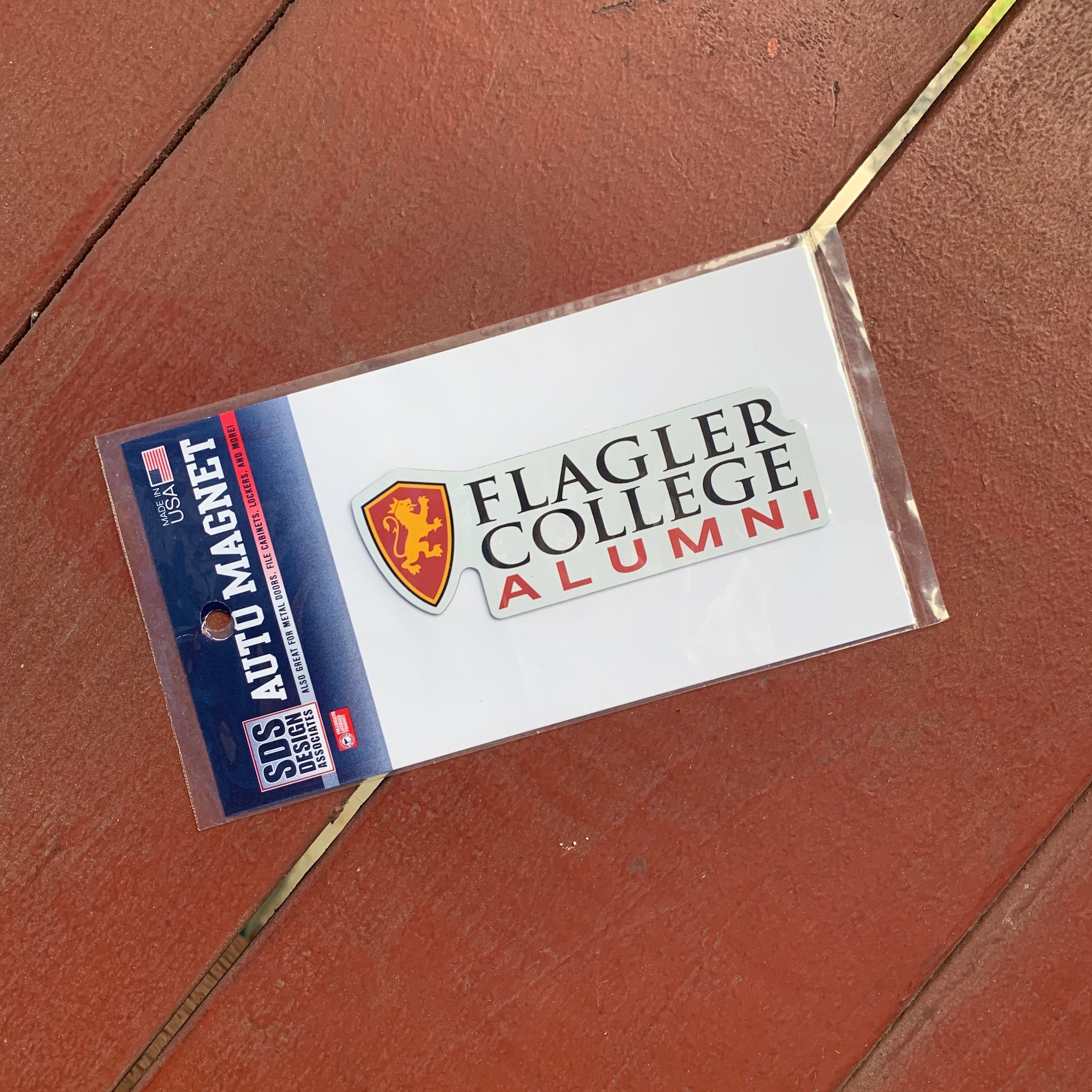 Auto magnet with Flagler College shield logo left of black lettering saying Flagler over College over red lettering saying Alumni