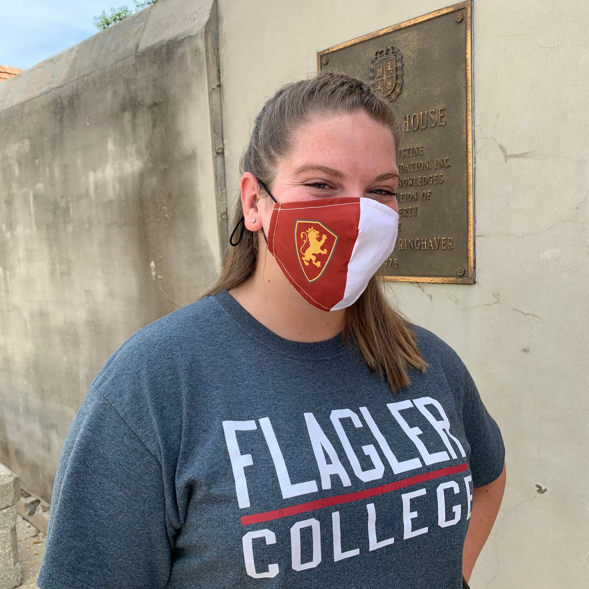 woman wearing face mask. Crimson on right side with Flagler College Shield Logo and white on left