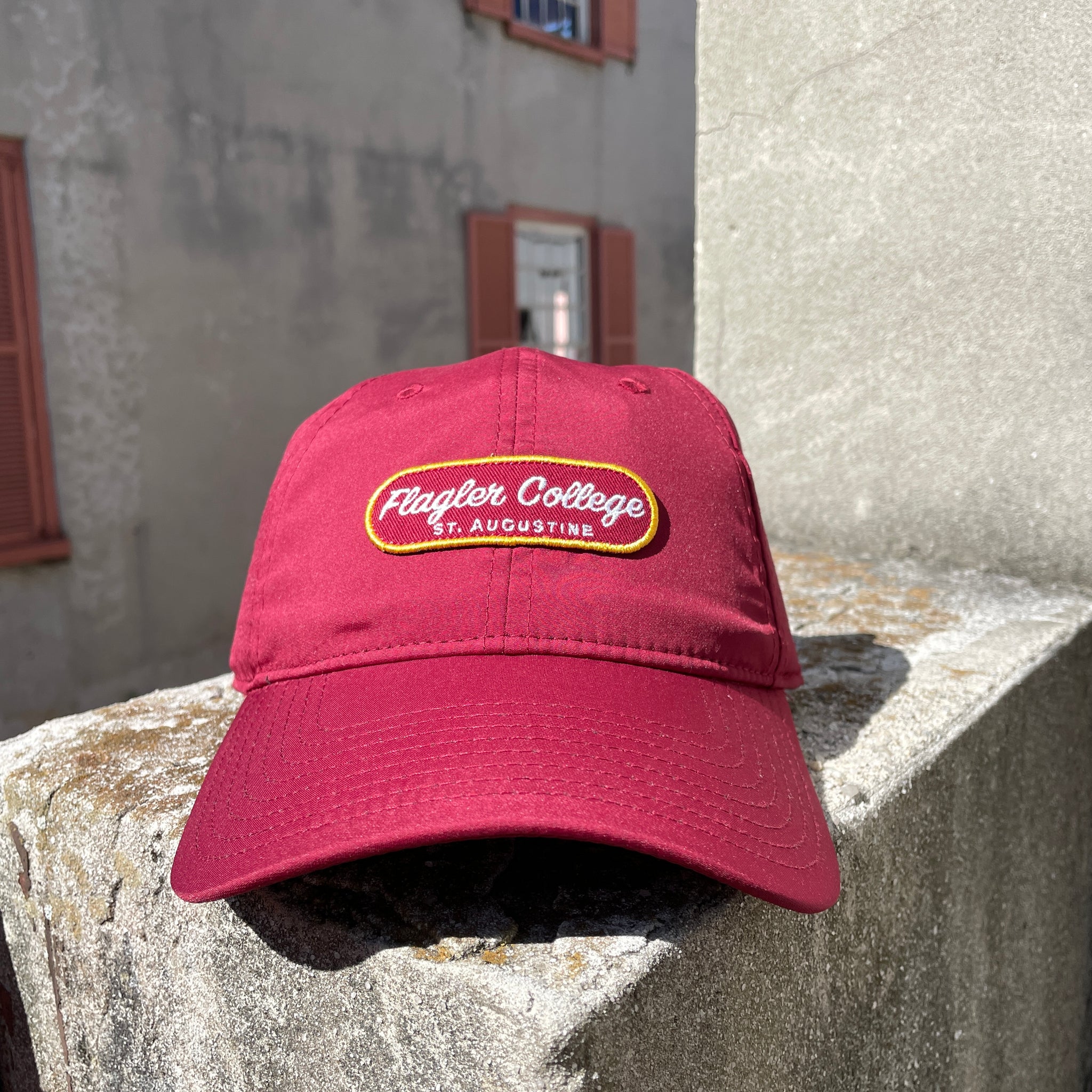 Crimson hat with crimson patch with yellow boarder and white cursive embroider saying Flagler College over print St. Augustine