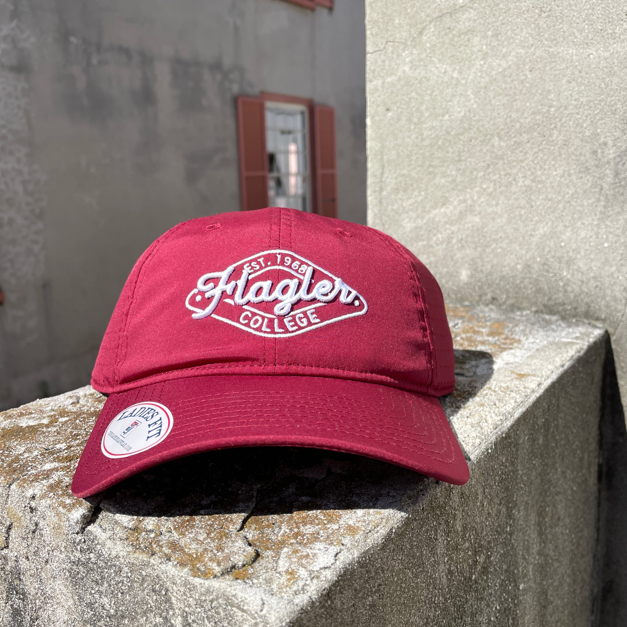 crimson side perforated hat with white letters saying est.1968 over cursive letters saying Flagler over print college all inside white diamond border