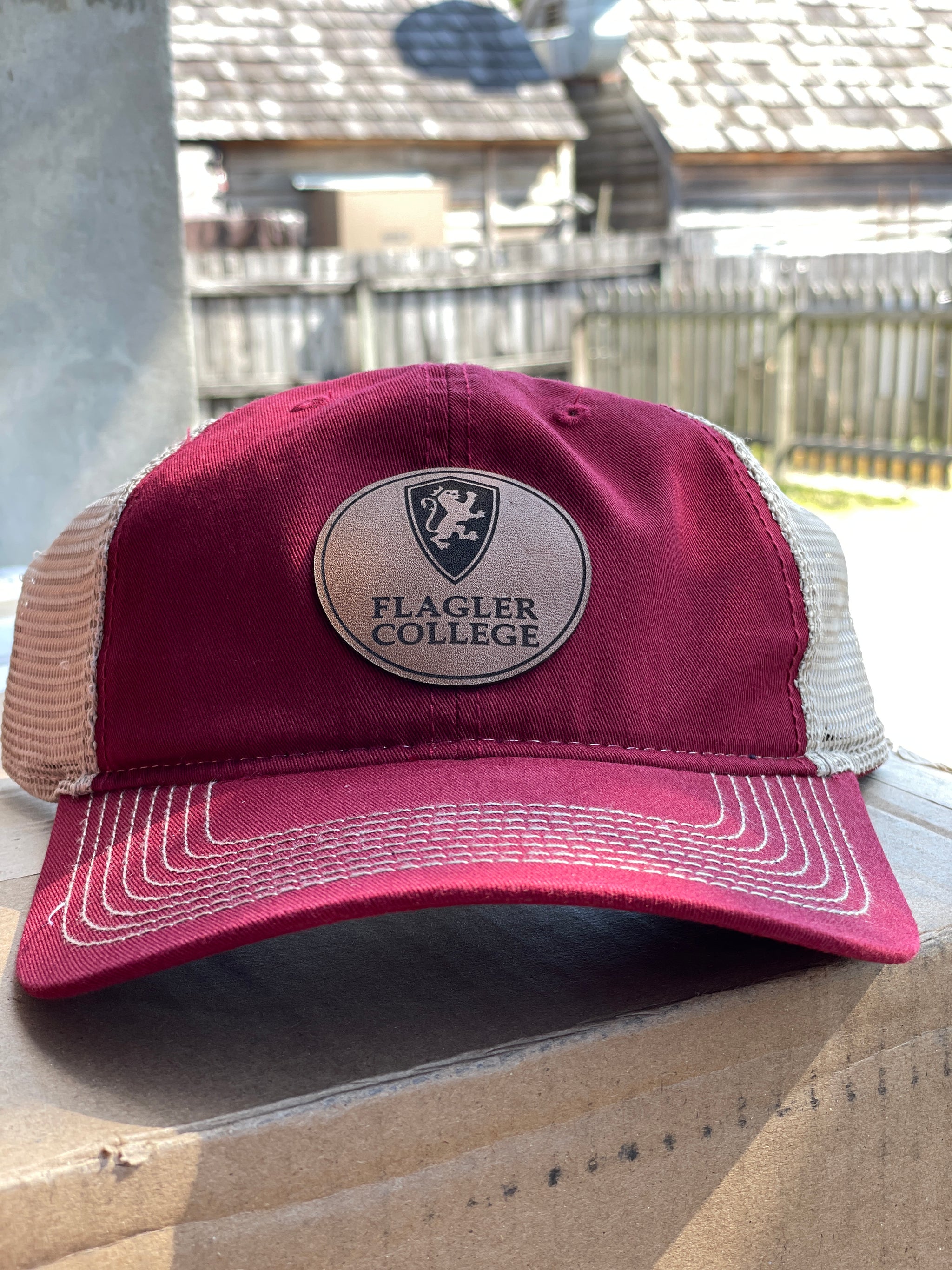 Crimson hat with brown mesh and patch in center with Black flagler shield logo over Black imprint saying Flagler over College