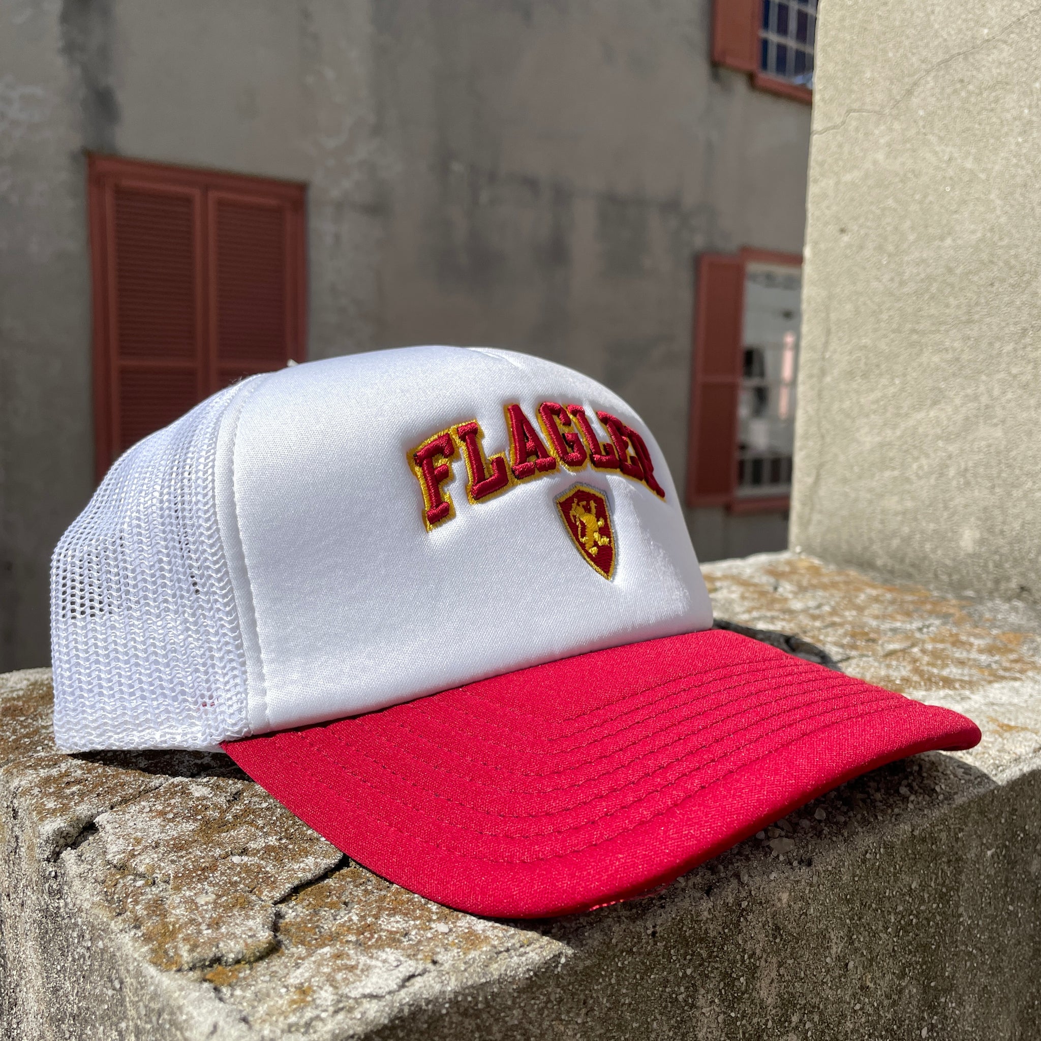 Red and White foam Trucker hat with red embroidering saying Flagler with yellow outline over Flagler shield logo