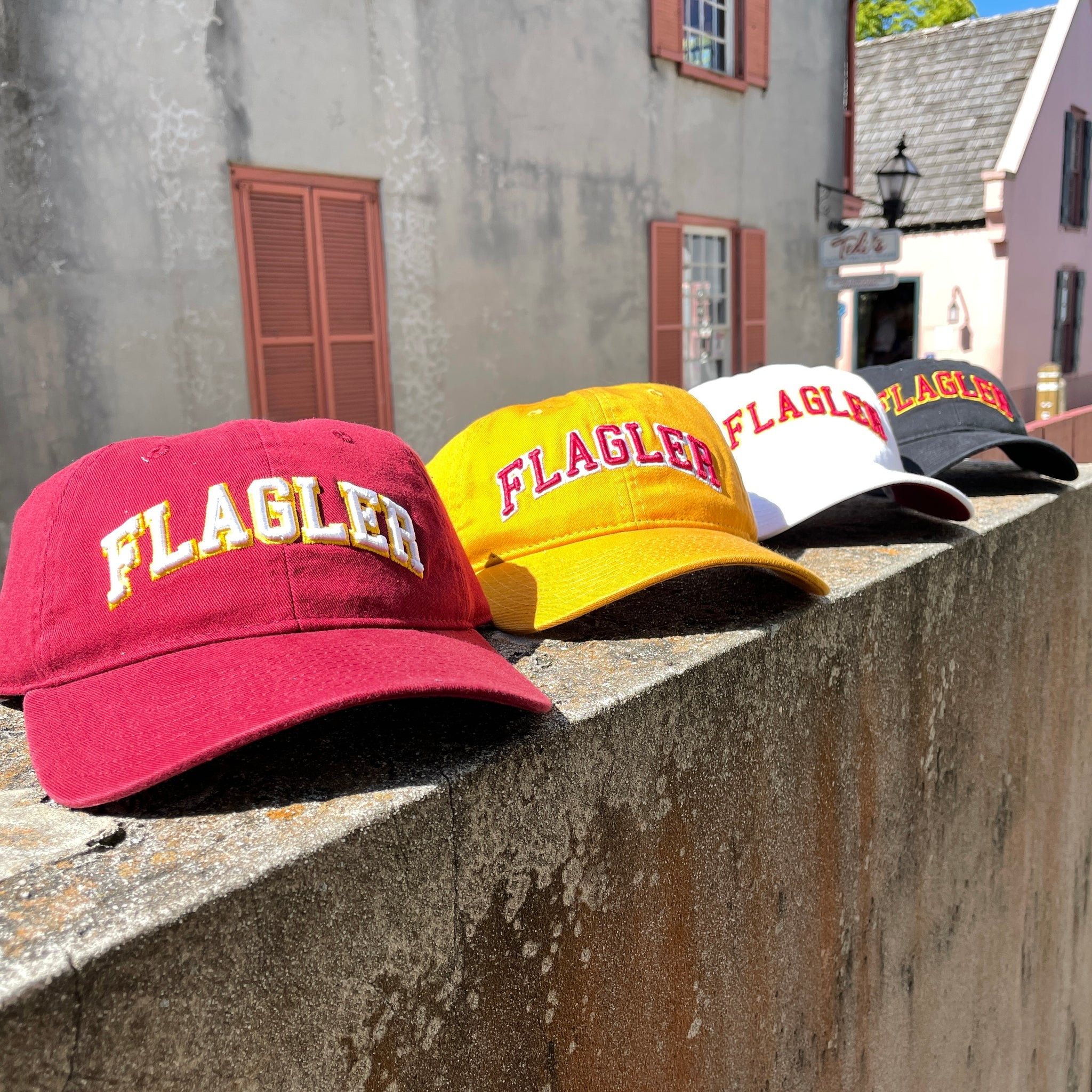 4 hats in photo. Crimson hat with white letters saying Flagler. Yellow Hat with red letters saying Flagler. White hat with red letters saying Flagler. Black hat with red letters saying Flagler