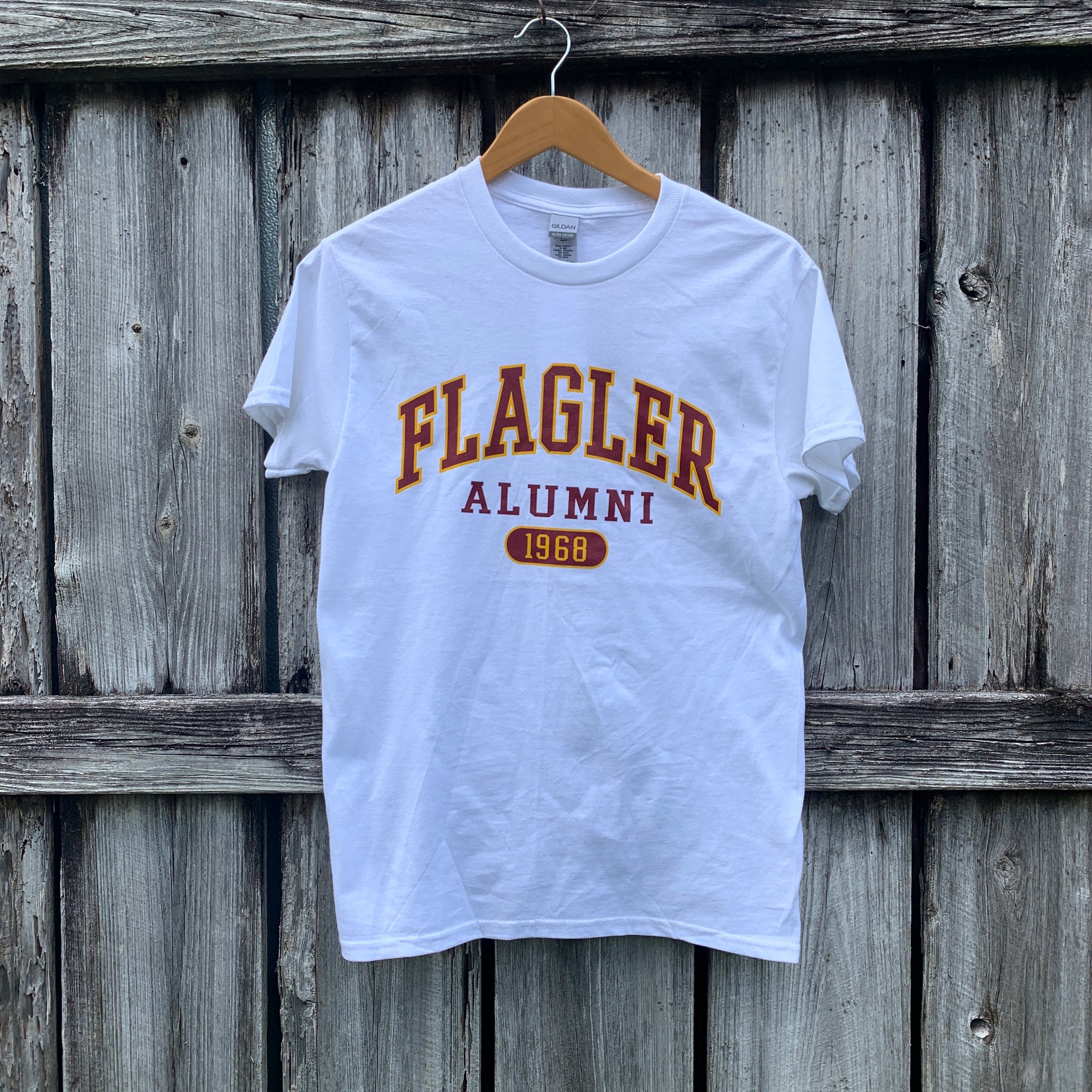 White t-shirt with crimson imprint saying Flagler over Alumni over crimson oval with yellow text saying 1968