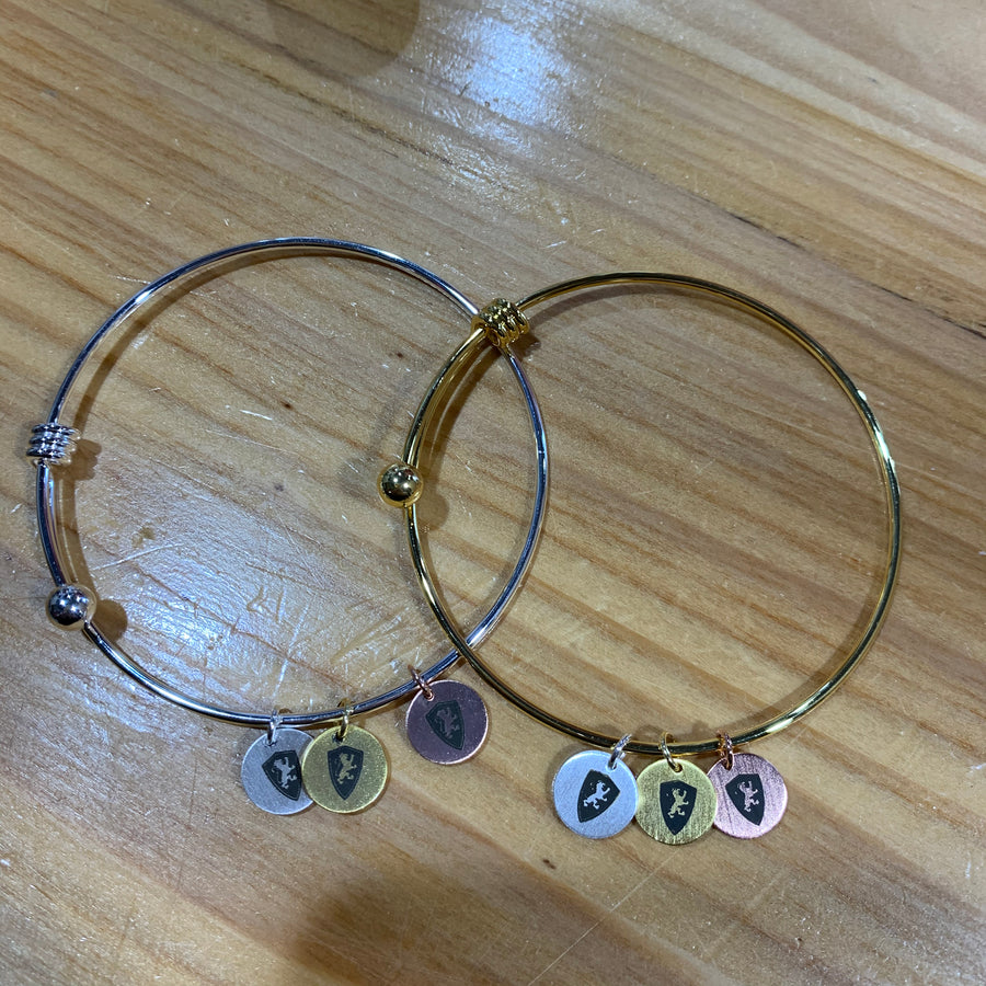 two bangle charm bracelets, one silver and one gold. each has three charms with black lion shields on each. the charms are rose gold, gold, and silver