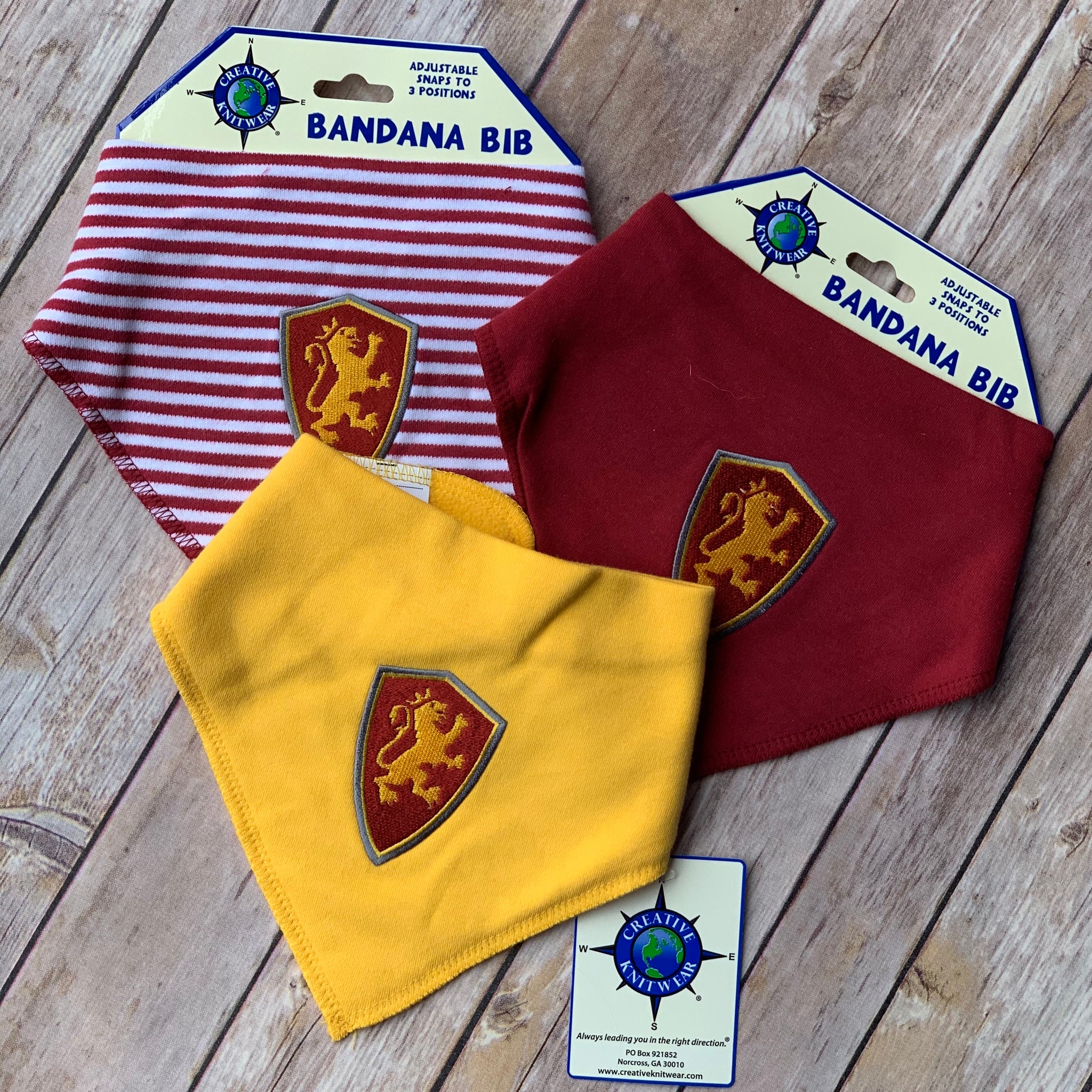 three bandanna bibs with red and yellow embroidered shield patch on front of each. The first big has red and white stripes, the second is solid yellow and the last is solid red